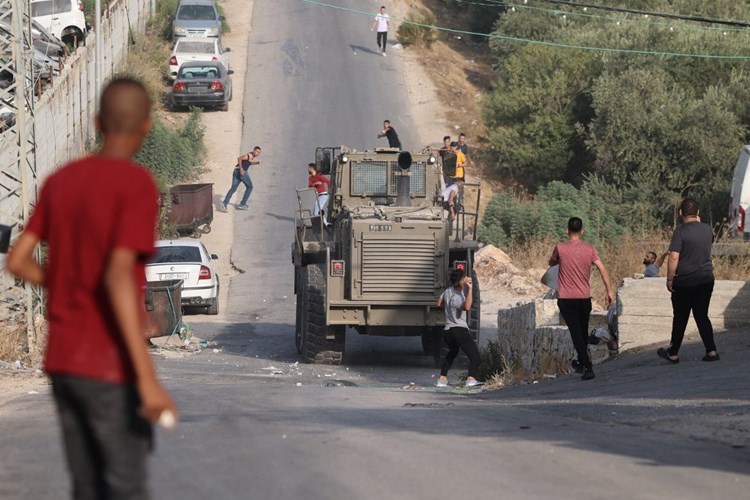 Jóvenes palestinos lanzan piedra contra un blindado israelí.